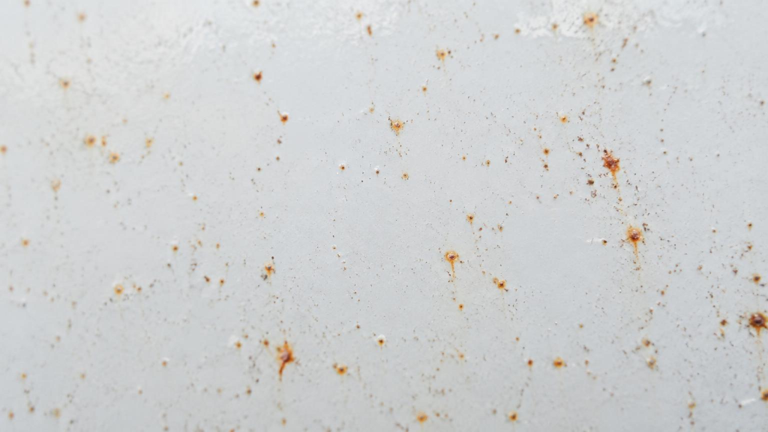 Macro close-up of tiny orange iron fallout specks embedded in white car paint