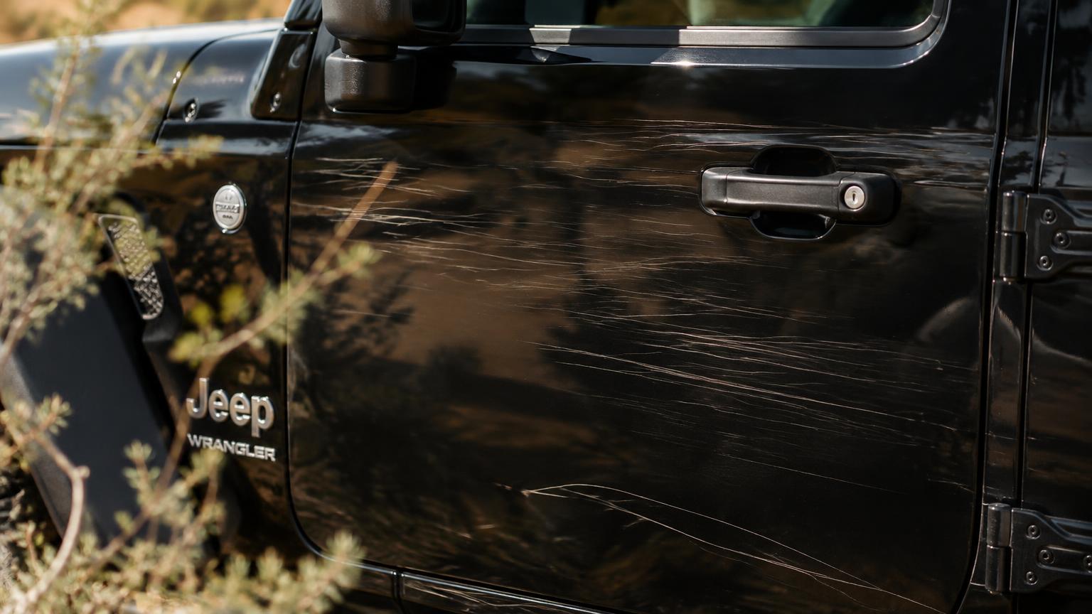 Close-up of desert pinstripe scratches on a black Jeep Wrangler door with desert brush in the foreground