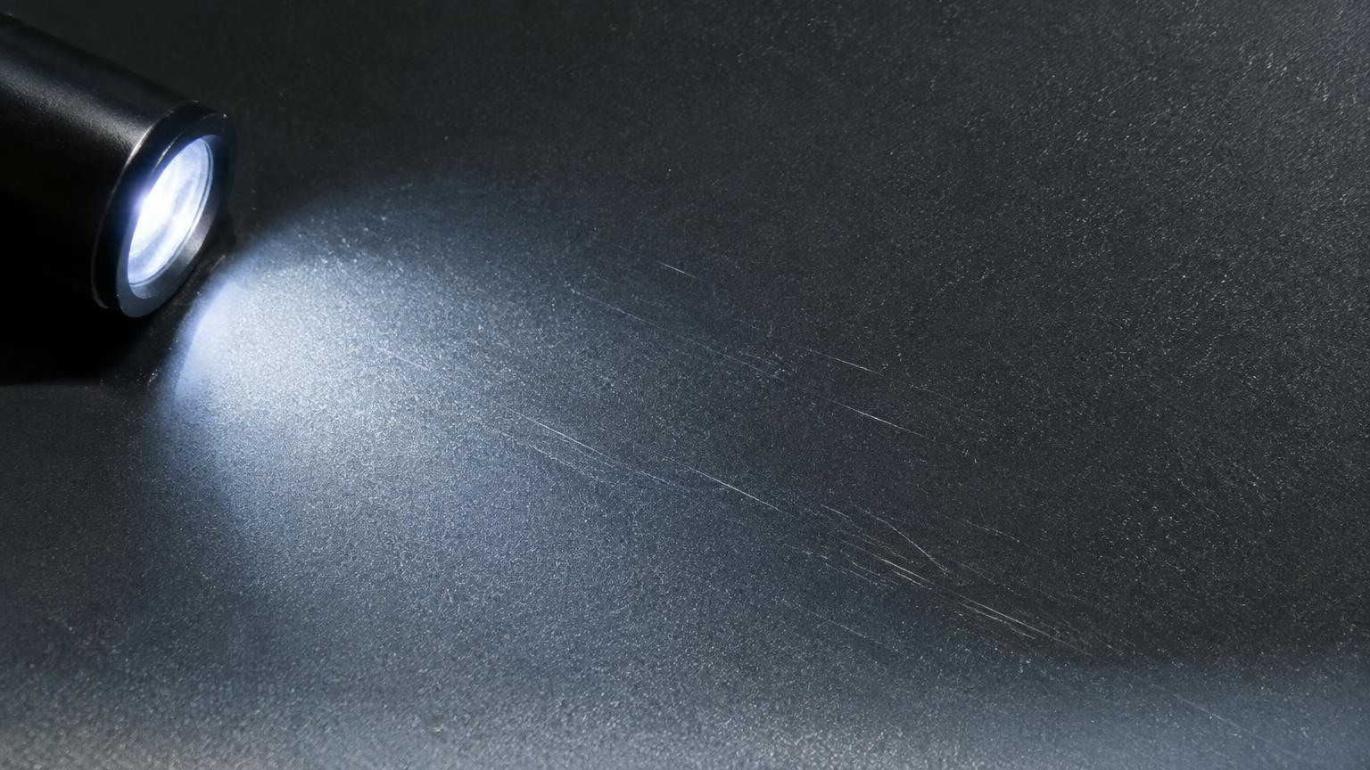 Flashlight held at a low angle revealing fine pinstripe scratches on dark grey truck paint