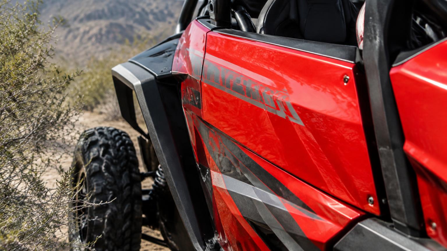 Close-up of a glossy red side-by-side door panel with graphics beside desert brush